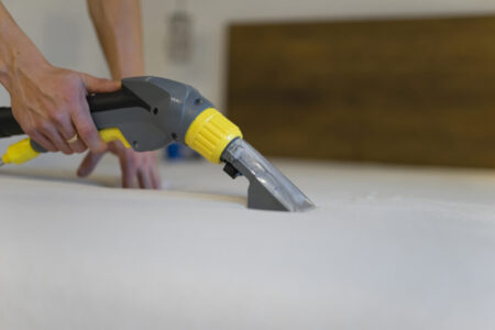 Employee of cleaning company cleans and disinfecting the mattress using a washing vacuum cleaner. Furniture dry cleaning process