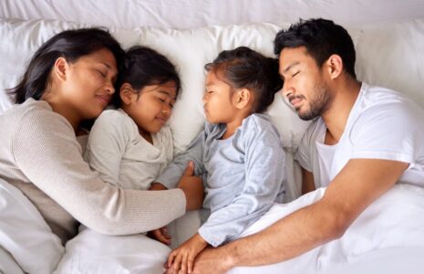 You couple resting peacefully with their children in a big soft bed at home.