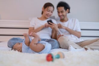 Mom and father use mobile phone enjoy online shopping baby happy laying on bed playing