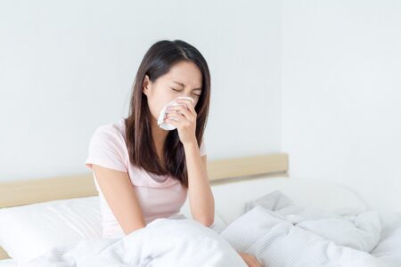 Woman sneezing on bed