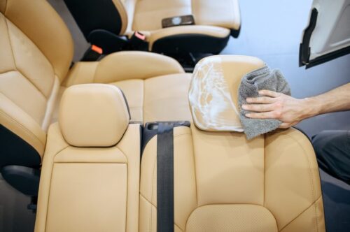 Worker with rag wipes removed car seat, top view, dry cleaning and detailing. Vehicle washing in garage, thoroughly care of automobile, chemical and vacuum clean service